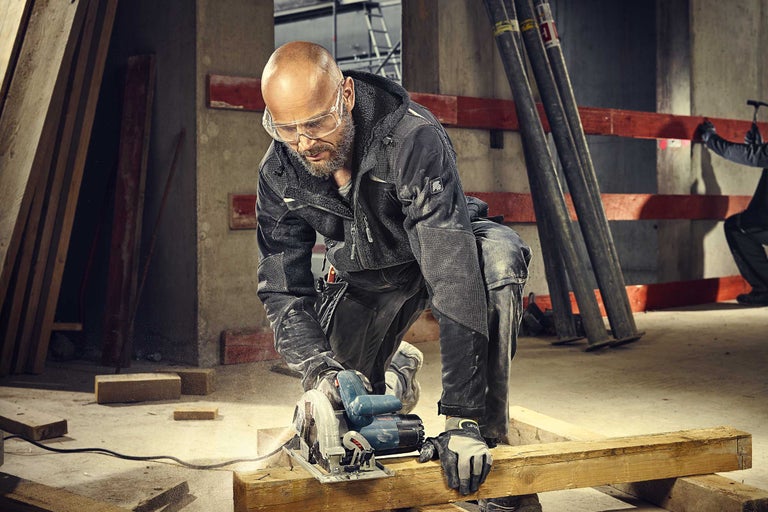 Handwerker beim Sägen von Holz mit einer Handkreissäge in einer Rohbauumgebung