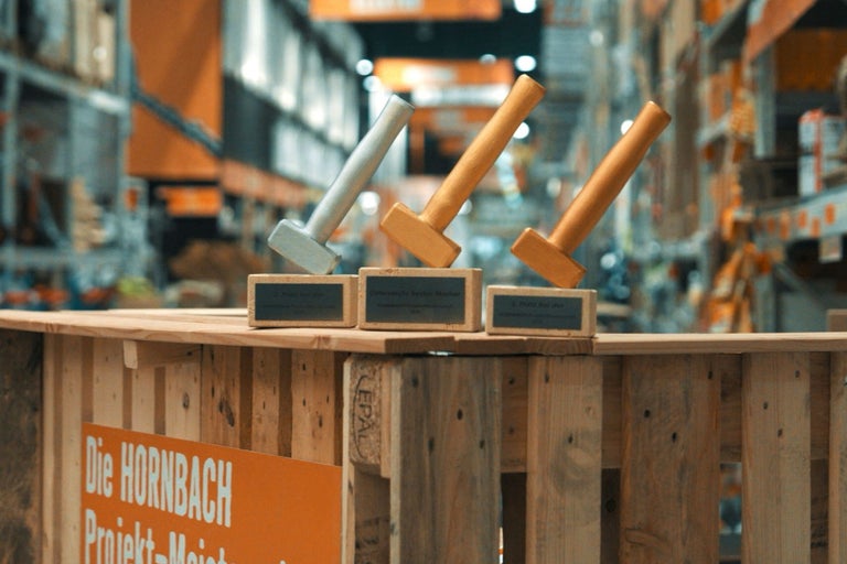 Drei Hammer-Pokale stehen auf einer Holzpalette in einem Hornbach Markt.