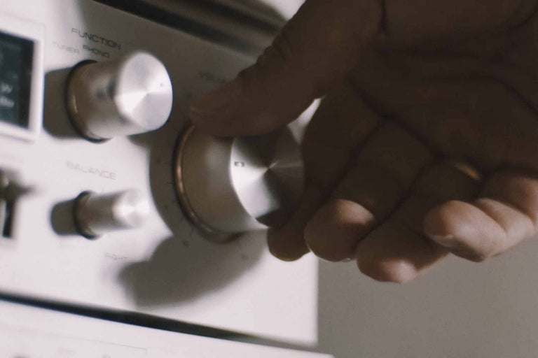 Detailaufnahme einer Hand, die an einem Lautstärkeregler eines Hi-Fi-Verstärkers dreht.