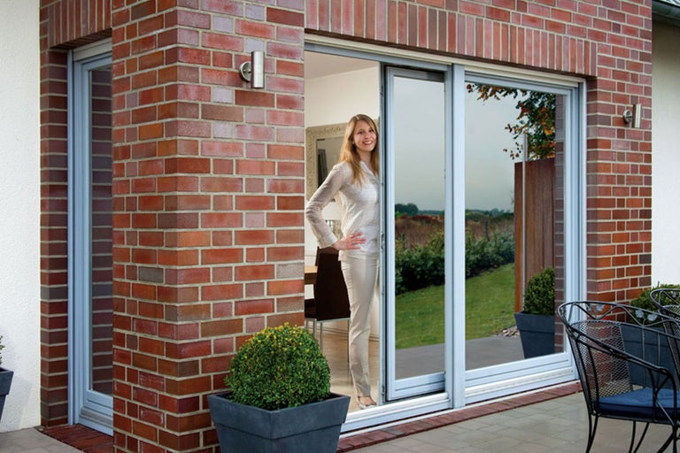 Terrassentür aus Glas mit Aluminiumrahmen in einem Haus mit Backsteinfassade und einer Frau im Hintergrund