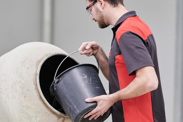 Ein Mann mit Schutzbrille gießt einen Eimer in einen Betonmischer.