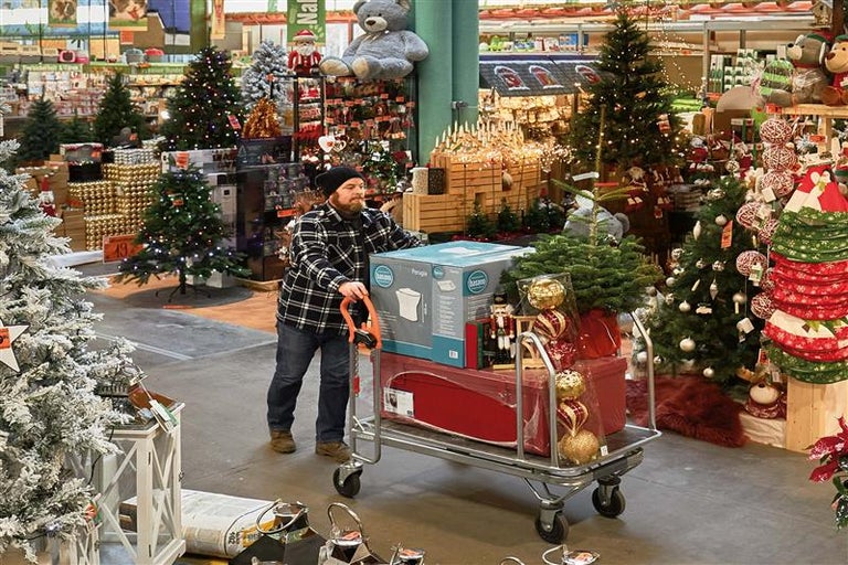Ein Mann schiebt einen Einkaufswagen mit Weihnachtsartikeln und einem Toilettenbecken durch einen Baumarkt.