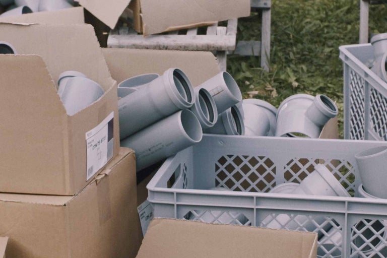 Graue Abwasserrohre und Formstücke in Kartons und einem Kunststoffbehälter.