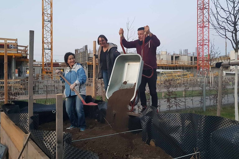 Personen füllen Erde in ein mit Noppenfolie ausgelegtes Beet mit einer Schubkarre und einem Spaten