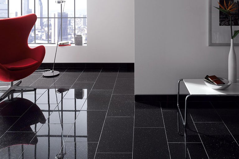 Innenraum mit Bodenfliesen in dunkler Optik, kombiniert mit einem roten Sessel und einem kleinen Beistelltisch.
