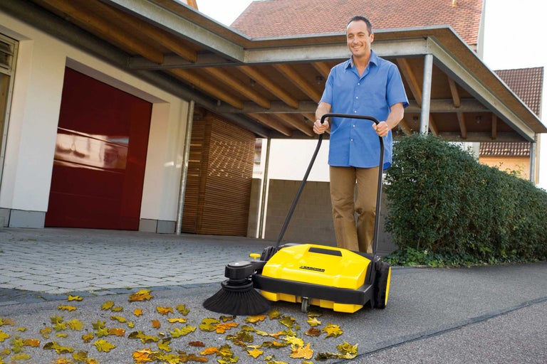 Mann benutzt eine gelbe Kehrmaschine zur Reinigung einer Auffahrt mit Blättern.