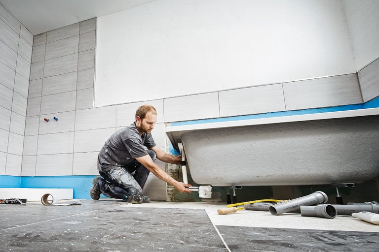 Handwerker montiert Badewanne im Badezimmer mit Fliesen