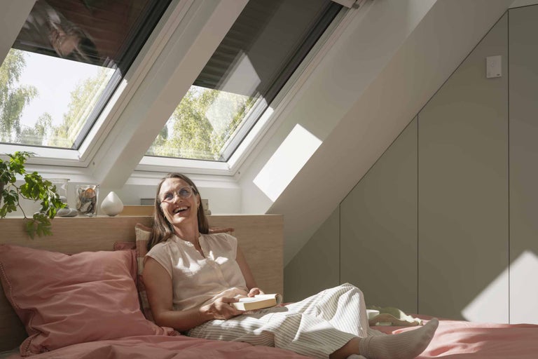 Helles Schlafzimmer mit Dachfenstern und einer Frau, die ein Buch liest