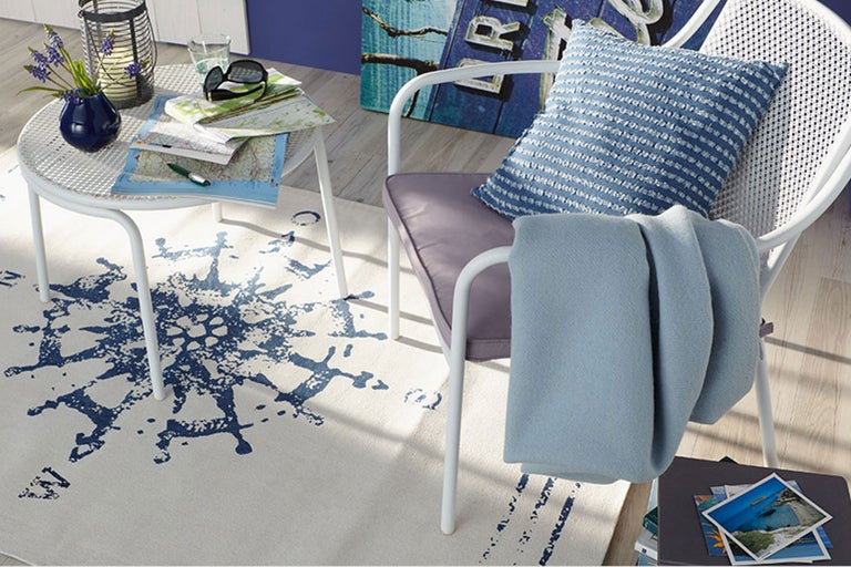 Dekoratives Wohnambiente mit weißem Stuhl, Beistelltisch, Teppich mit Kompassmuster und Accessoires