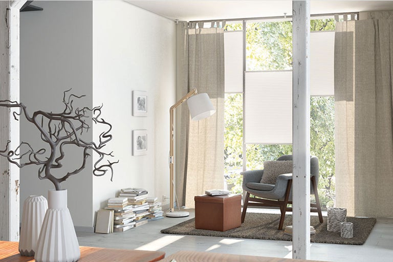 Wohnzimmer mit Sessel, Vorhängen und Plissee-Rollos