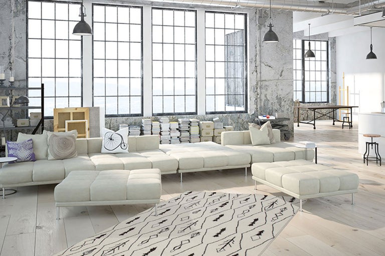 Geräumiges Wohnzimmer mit modularem Sofa, Teppich und großen Fenstern im Loft-Stil.