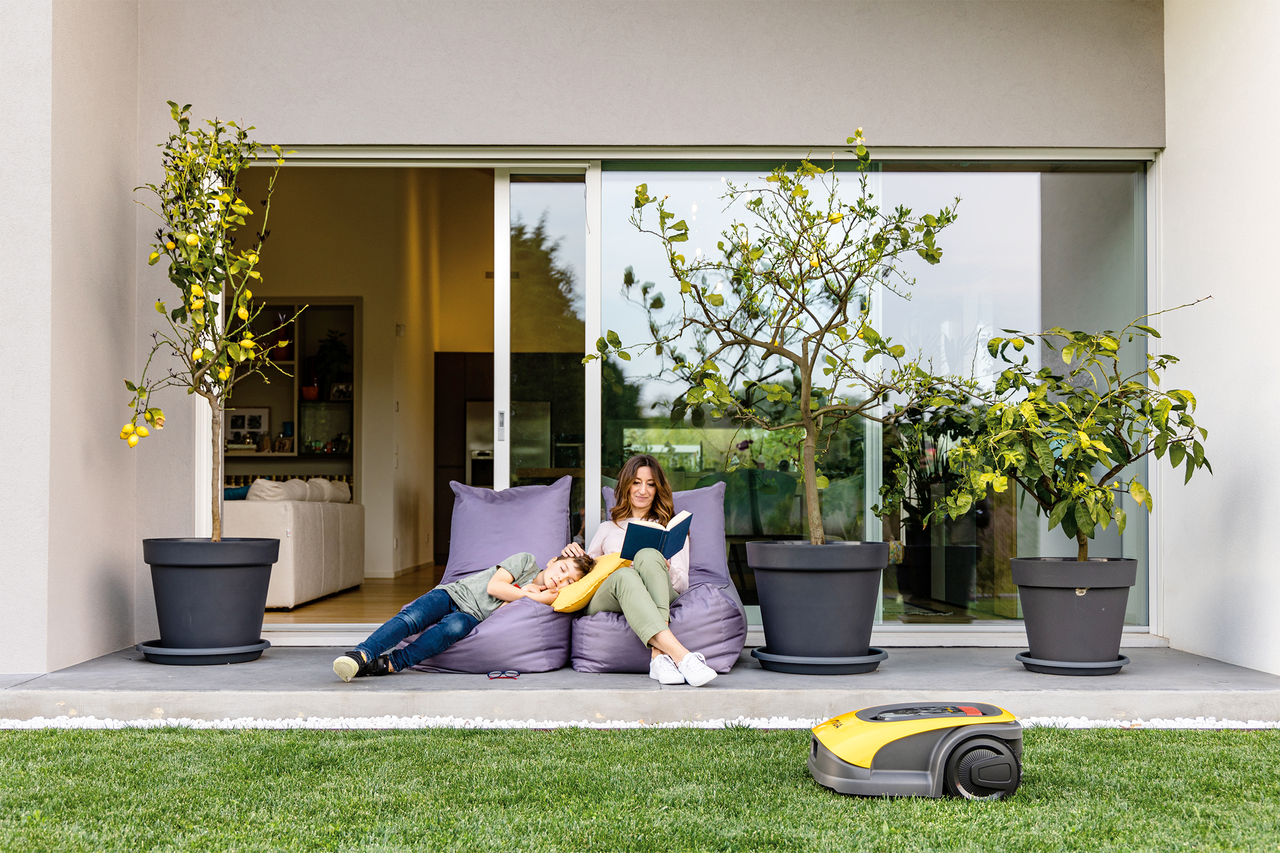 Szene im Garten mit Mutter, Kind, Zitronenbäumen und Rasenmähroboter