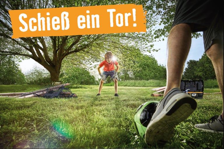 Szene im Garten mit Kind, Tor und Werkzeugkasten. Spruch: Schieß ein Tor!