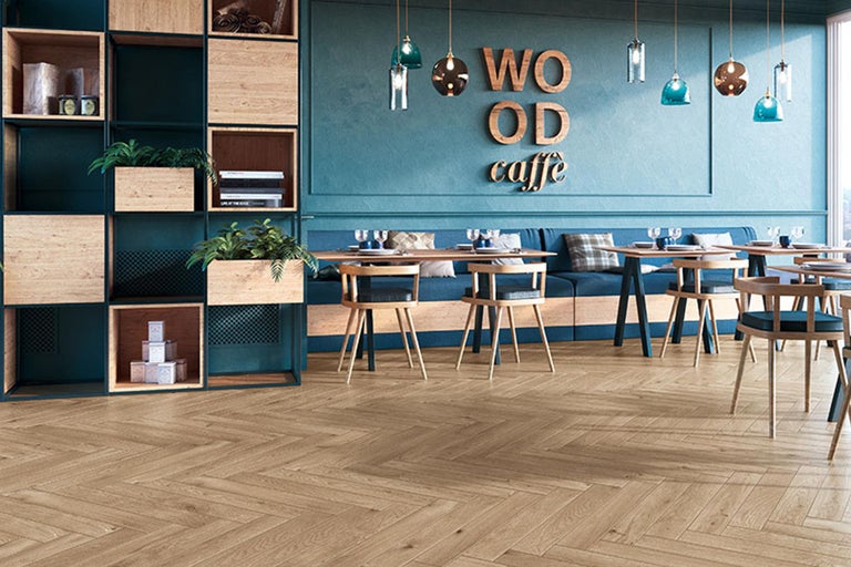 Innenraum eines Cafés mit Holzboden in Fischgrätmuster, Tischen, Stühlen und einem Regal