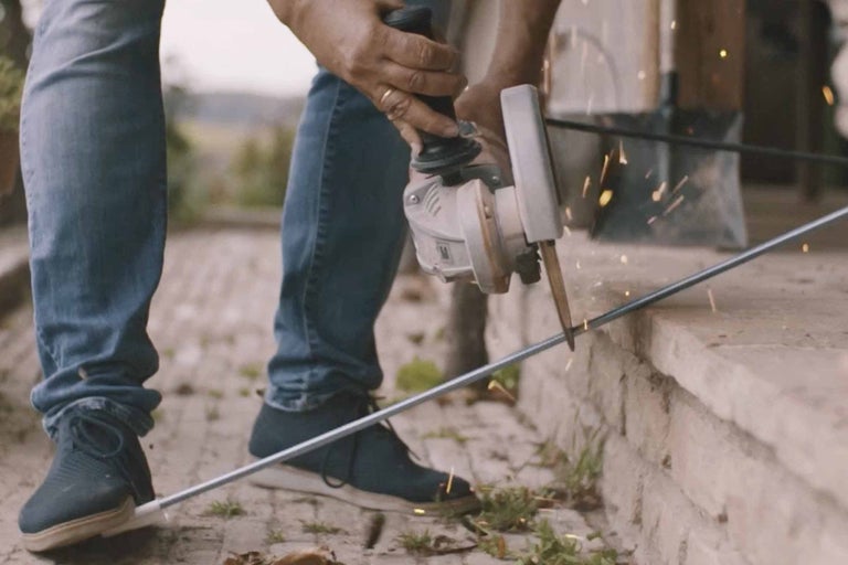 Eine Person schneidet mit einem Winkelschleifer eine Stange.