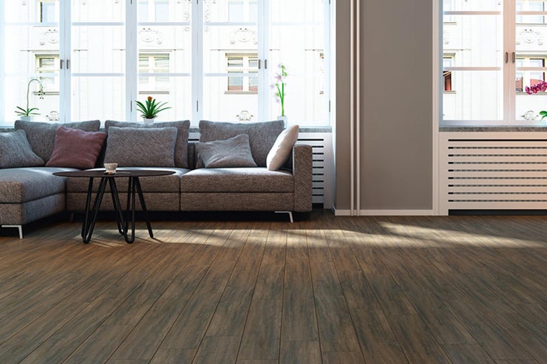 Heller Wohnraum mit braunem Laminatboden, grauer Couch und Tisch