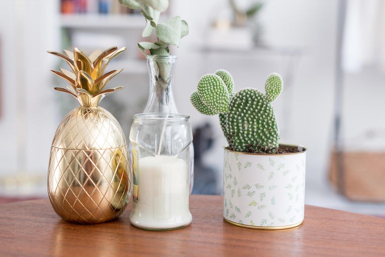 Dekorative Anordnung mit goldener Ananas, Kerze im Glas und Kaktus im Topf auf einem Tisch.