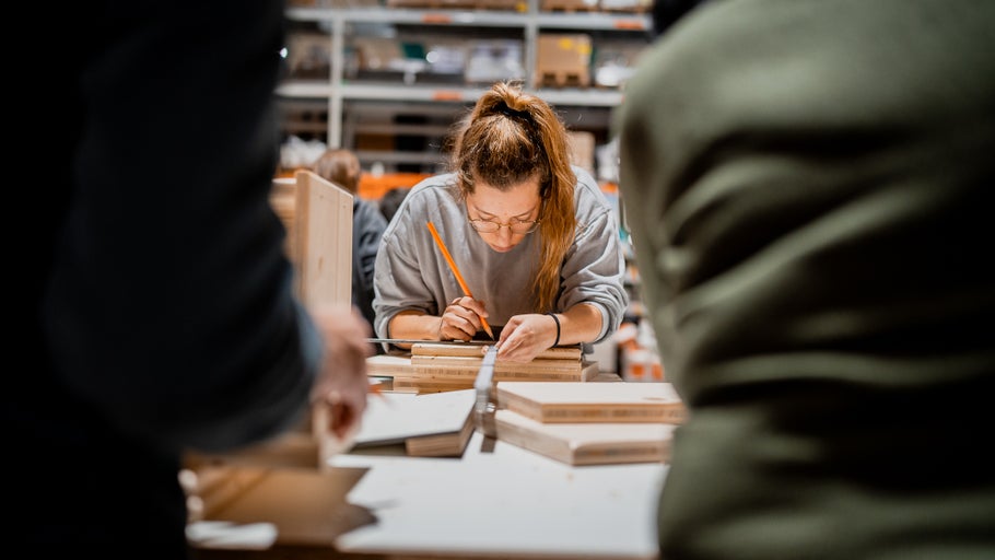 Frau zeichnet mit Bleistift und Lineal auf Holzstücke im Baumarkt