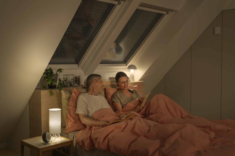 Ein Paar liest im Bett unter Dachfenstern, beleuchtet von Nachttischlampen.