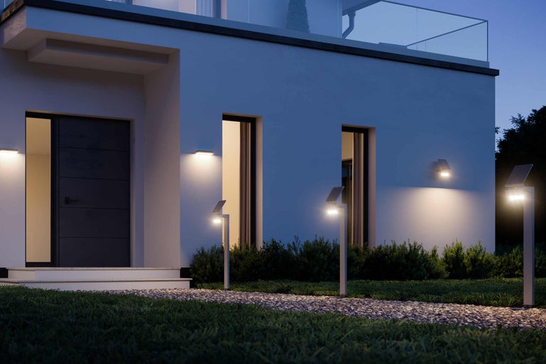 Außenansicht eines Hauses mit Solarleuchten entlang eines Kieswegs und Wandleuchten neben der Haustür und Fenstern