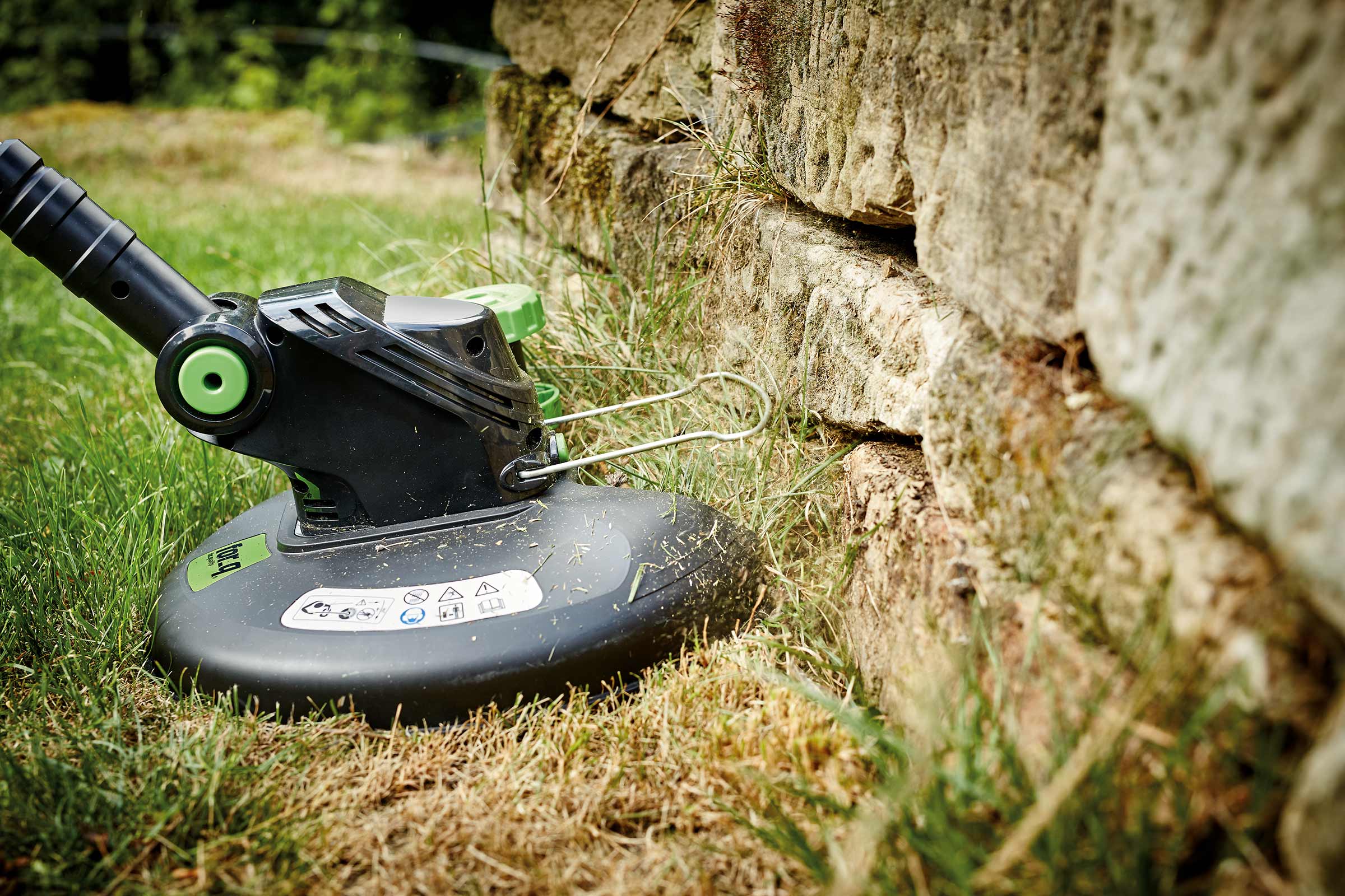 Rasentrimmer zum Kantenschneiden an einer Steinmauer