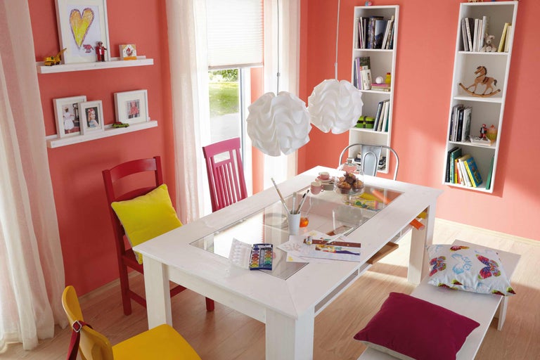 Helles Kinderzimmer mit Esstisch, Stühlen, Regalen und Dekorationen.