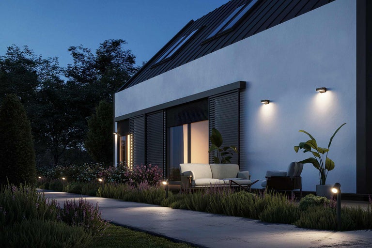 Außenansicht eines modernen Hauses mit Gartenbeleuchtung und Gartenmöbeln in der Abenddämmerung.