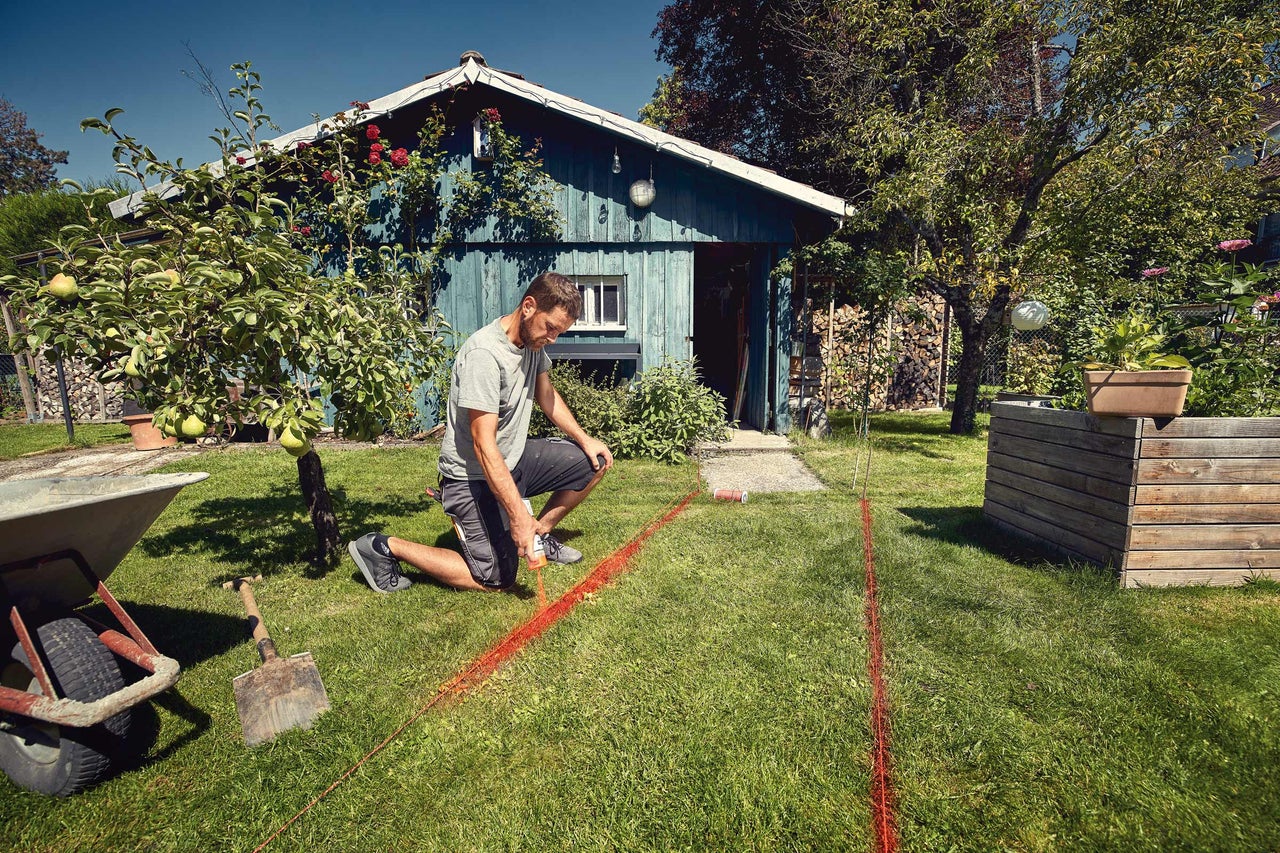 Mann markiert Bereich im Garten mit Richtschnur vor Gartenhaus