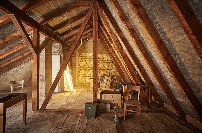 Dachboden mit Holzbalken, Ziegelwänden, Leiter und verschiedenen Gegenständen.