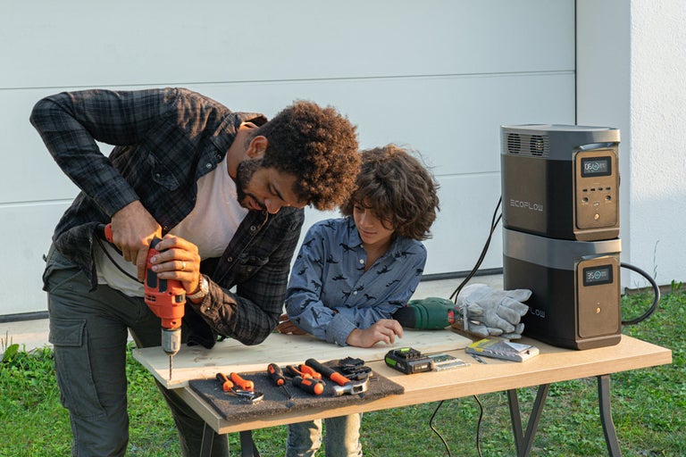 Vater bohrt mit seinem Sohn ein Loch in ein Brett auf einem Tisch, mit EcoFlow Powerstation