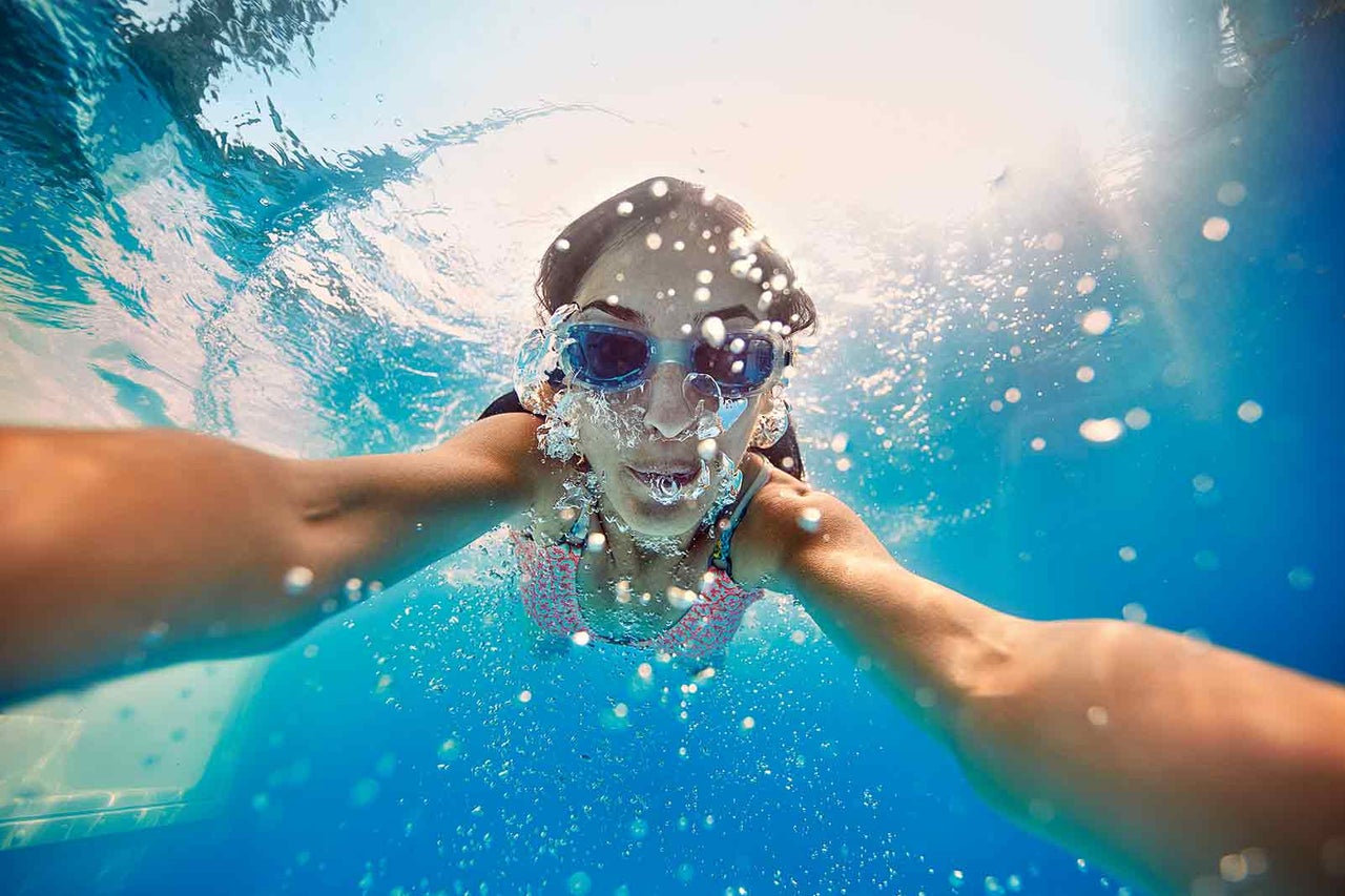 Frau schwimmt mit Schwimmbrille im Schwimmbad unter Wasser.