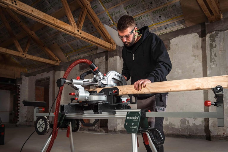 Mann arbeitet mit einer Metabo Kappsäge und einem Metabo Sägetisch an einem Holzbrett.