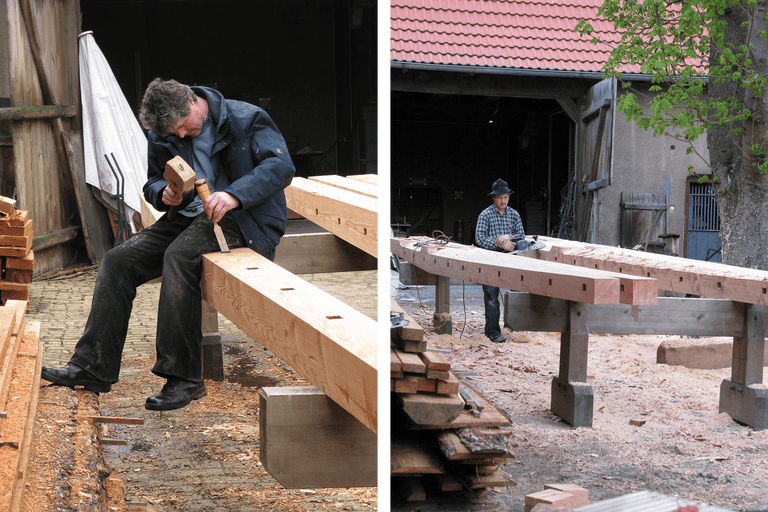 Zwei Handwerker bearbeiten Holzbalken mit Werkzeugen in einer Werkstatt.