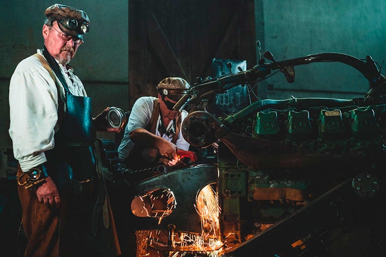 Zwei Handwerker arbeiten an einer alten Maschine mit einer Flex und Schutzbrille