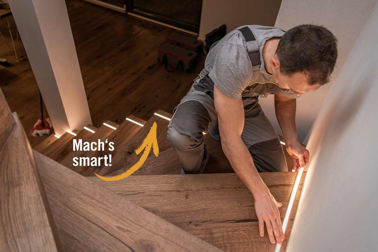 Ein Handwerker befestigt LED Streifen an einer Holztreppe.