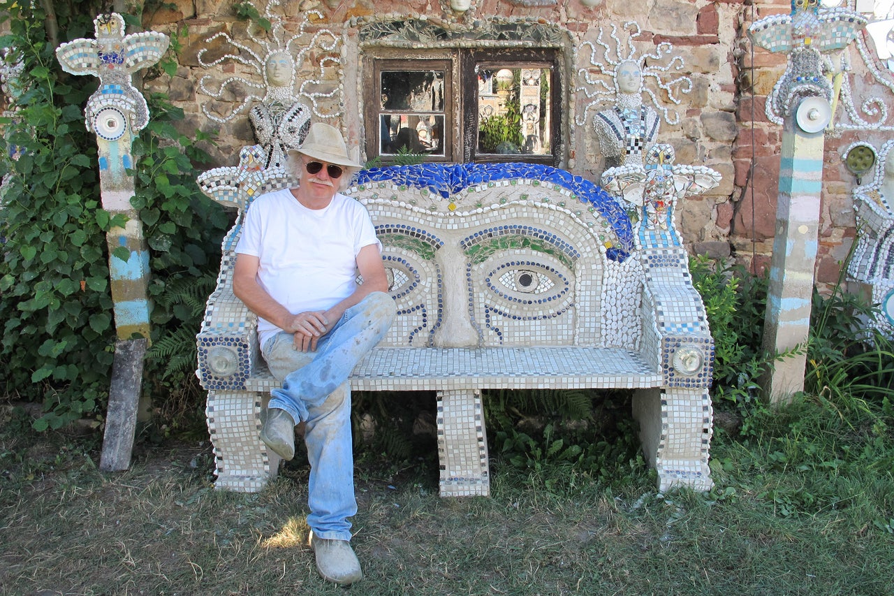 Mann sitzt auf einer mit Mosaiken verzierten Bank vor einem Gebäude mit Mosaikdekoration.