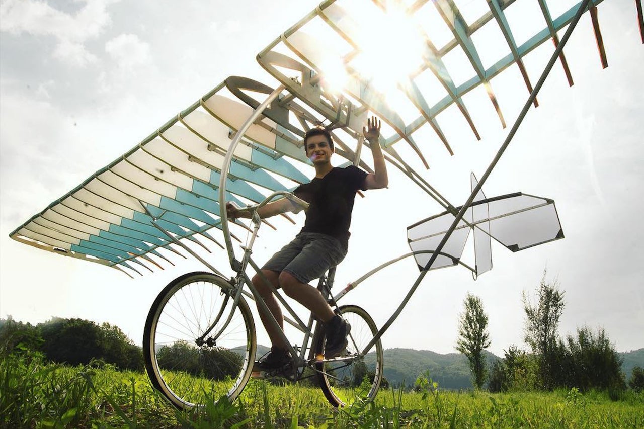 Ein Mann fährt ein Fahrrad mit Flügeln in einer grünen Landschaft.
