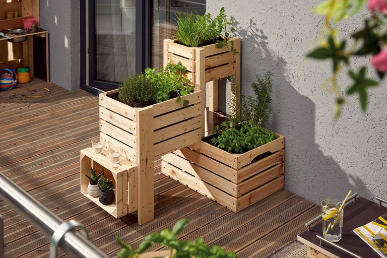 Mehrstufiges Kräuterbeet aus Holzkisten auf einem Balkon mit Holzboden.