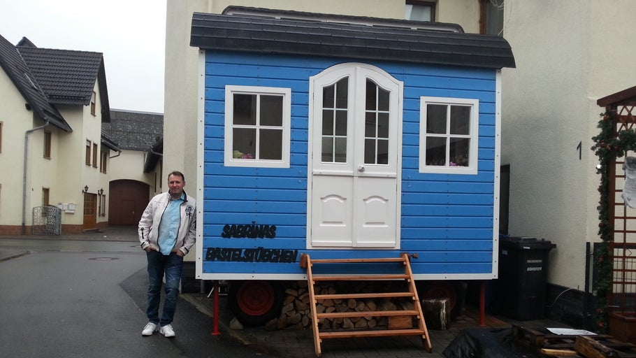 Blaues Bauwagen-Häuschen mit Fenstern und Tür sowie Holztreppe