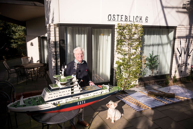 Mann mit Schiffsmodell und Hund vor Haus mit der Aufschrift 'OSTERBLICK 6'