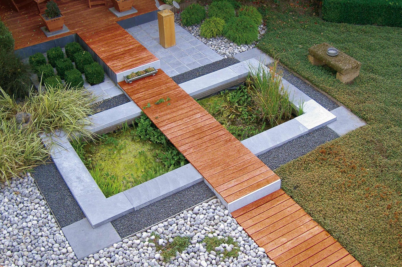Ansicht eines Gartenteichs mit Holzsteg, umgeben von Steinen und Pflanzen
