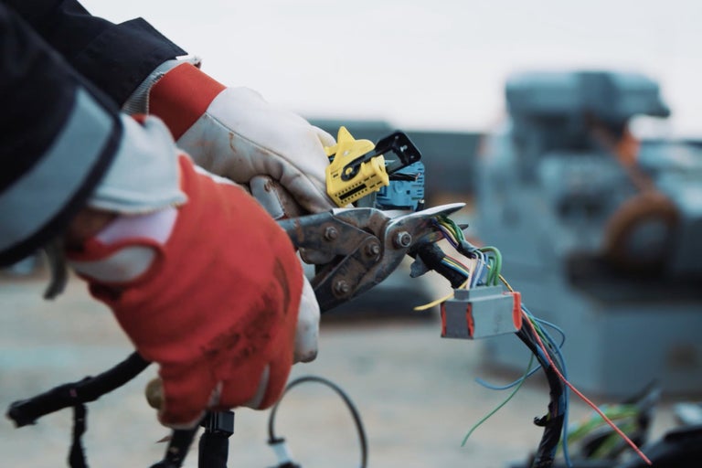 Ein Elektriker mit Arbeitshandschuhen trennt mit einer Zange Kabel.