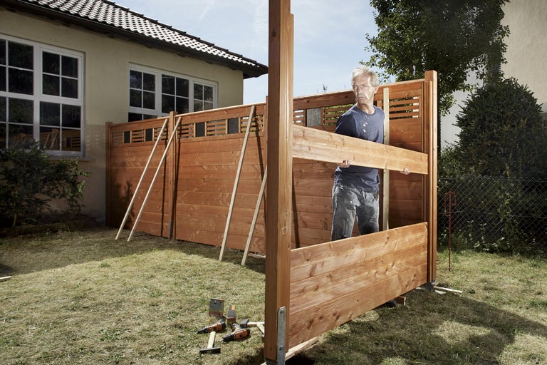 Mann baut einen Holzsichtschutz im Garten auf