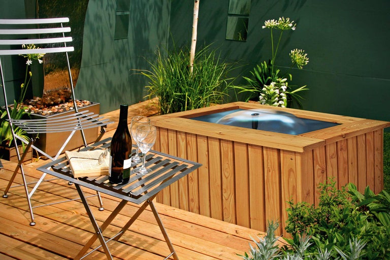 Szene mit Gartenmöbeln, Whirlpool, Weinflasche und Gläsern auf einer Holzterrasse