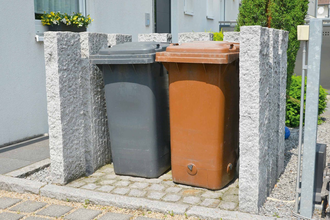 Zwei Mülltonnen in einer Mülltonnenbox aus Stein