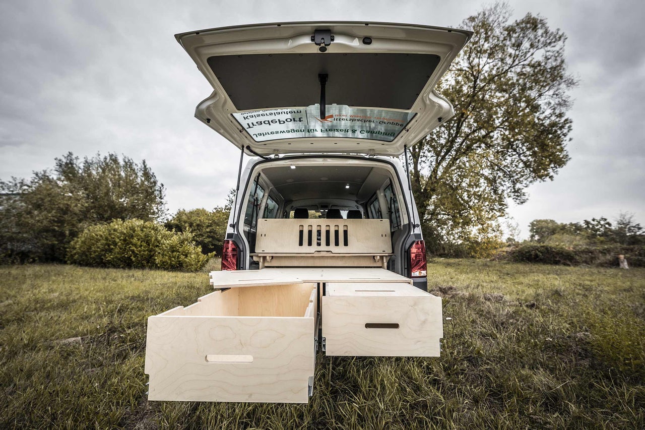 Heckansicht eines Campingbusses mit offenem Kofferraum und eingebautem Holzschranksystem mit Schubladen