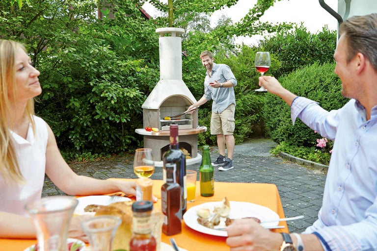 Szene im Garten mit Personen beim Grillen an einem Gartengrill und an einem Gartentisch sitzend