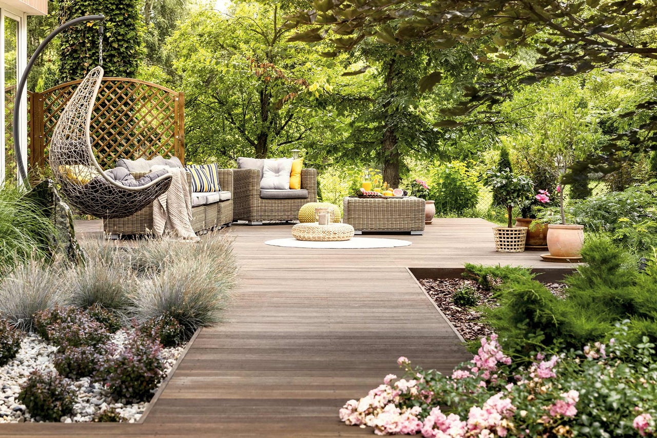 Gartenlounge-Set mit Hängesessel, Sofa, Tisch und Pflanzen auf einer Holzterrasse