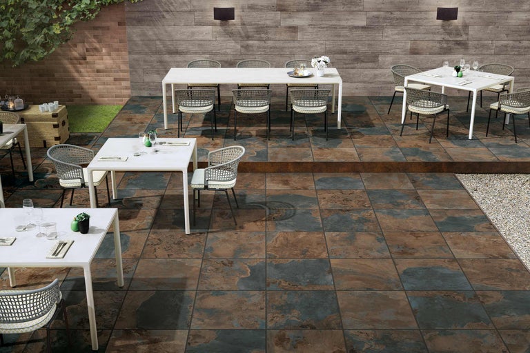 Terrasse mit Bodenfliesen, Tischen und Stühlen im Außenbereich.