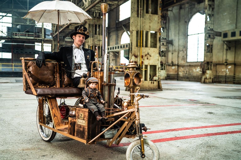 Mann im Steampunk-Outfit auf einem dekorierten Dreirad